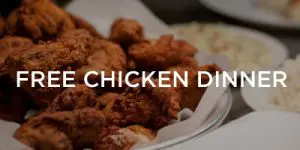 Plate of fried chicken pieces on a white platter with side dishes in the background; text overlay reads "FREE CHICKEN DINNER.