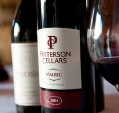A bottle of Patterson Cellars Malbec wine, vintage 2006, is placed next to a wine glass and another wine bottle in the background.
