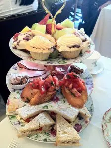 Three-tiered tray with assorted fresh fruit, cupcakes, and pastries on top; bruschetta and nuts in the middle; and assorted tea sandwiches on the bottom.